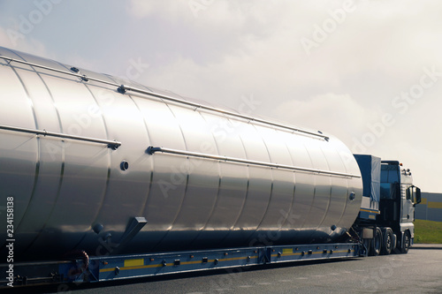 A view of a truck, a low-loader semi-trailer and an oversized cargo in the parking lot.