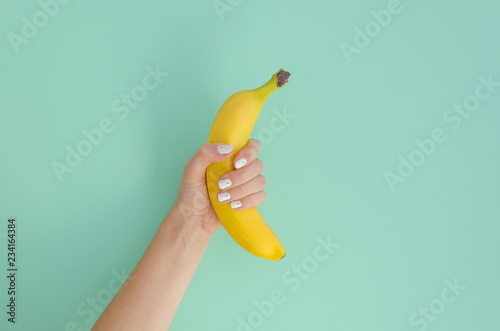 Female hand holding a banana on a mint background. Minimal fruit concept.