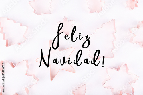 Flatlay with selection of holiday copper cookie cutters on white sparkling background. Holiday, Christmas card concept. Cozy homey details. Holiday wording in Spanish
