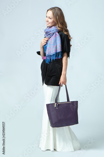 Stylish beautiful woman wearing a scarf around her neck holding a fashionable handbag in her hand. Studio photography on a blue background. Vertical orientation. photo