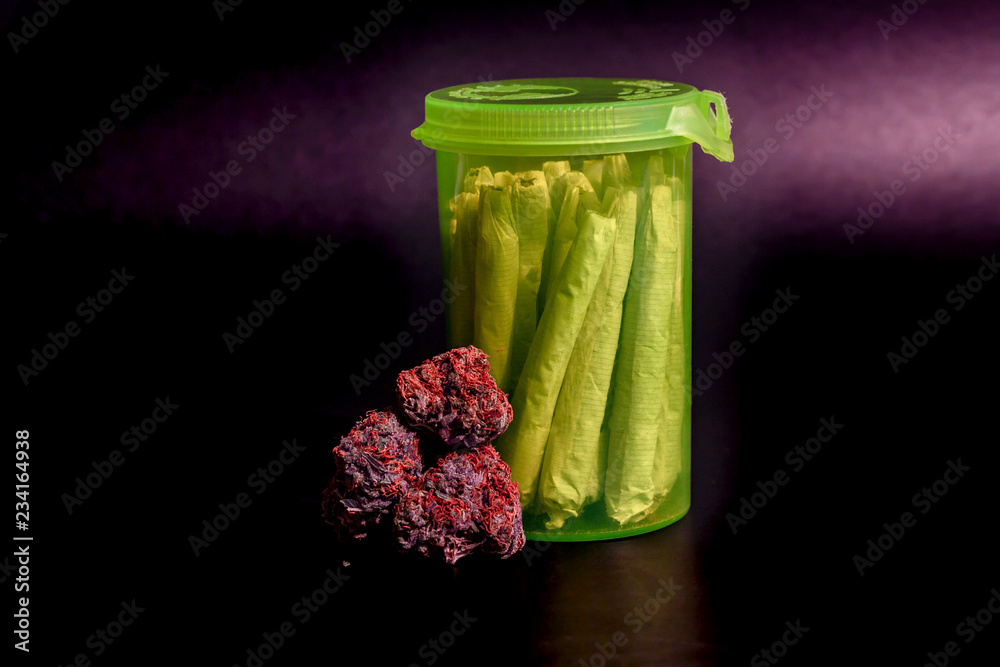 A bright transparent green RX pill bottle filled with marijuana joints next to a pile of purple buds with long red hairs.