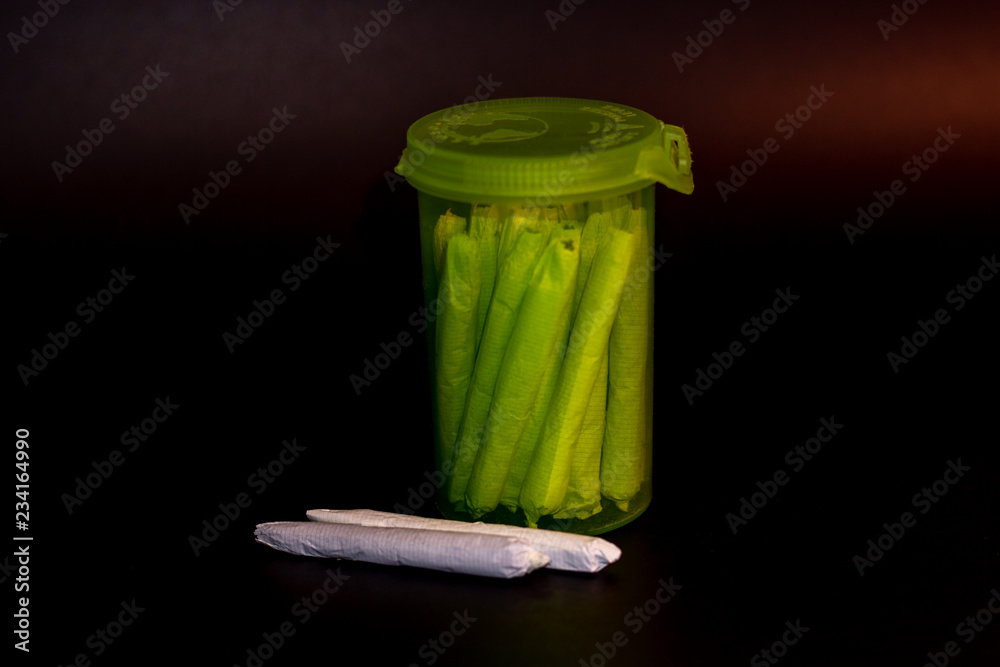 A bright transparent green RX pill bottle filled with marijuana joints with 2 joints laying next to it.