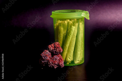 Obraz na płótnie A bright transparent green RX pill bottle filled with marijuana joints next to a pile of purple buds with long red hairs. w salonie