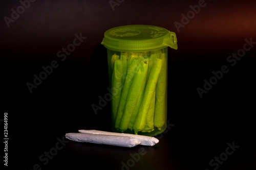 Obraz na płótnie A bright transparent green RX pill bottle filled with marijuana joints with 2 joints laying next to it. w salonie