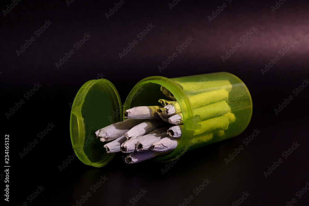 A bright transparent green RX pill bottle filled with marijuana joints laying on its side open.