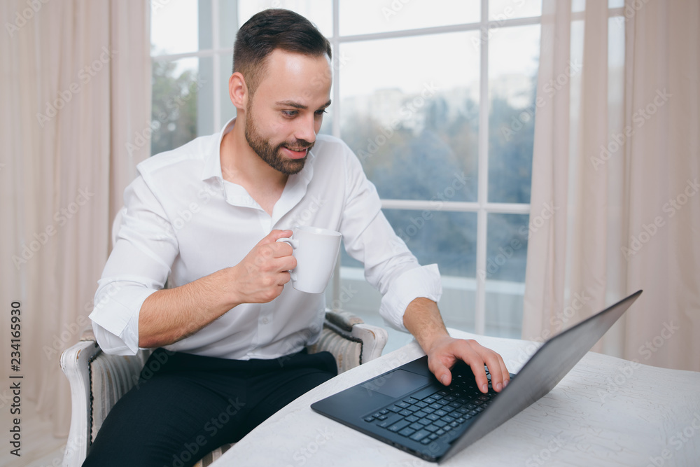 Young businessman with coffee in hand, use laptop on window background Young businessman with coffee in hand, use laptop on window background