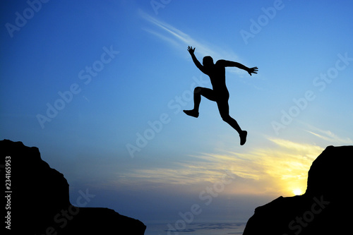 Man silhouette leaping on cliff on sunrise, success concept