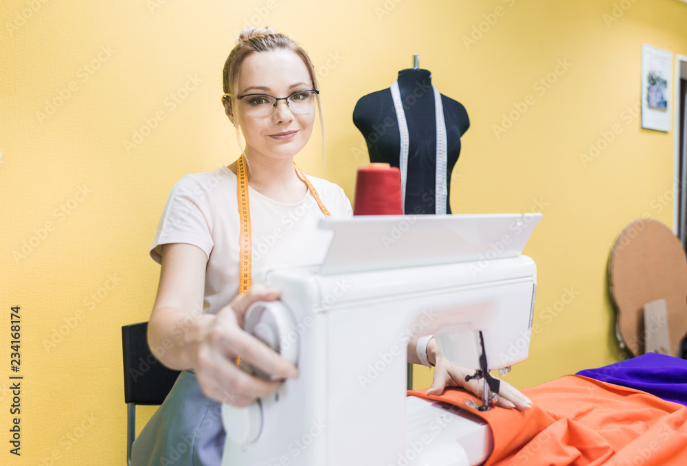 Sewing workshop. Seamstress at work. Young woman working with sewing machine on a colored background Sewing workshop. Seamstress at work. Young woman working with sewing machine on a colored background