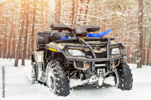 Close-up ATV 4wd quad bike in forest at winter. 4wd all-terreain vehicle stand in heavy snow with deep wheel track. Seasonal extreme sport adventure and trip. Copyspace