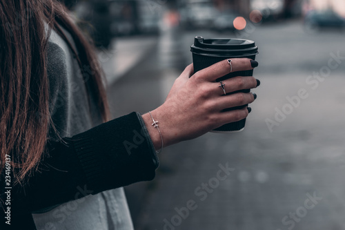 Woman hand with aircraft accessory hold black coffee on city background.