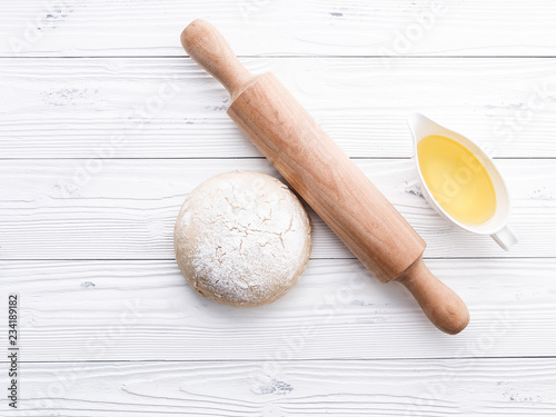 Raw pizza dough and rolling pin on wooden background