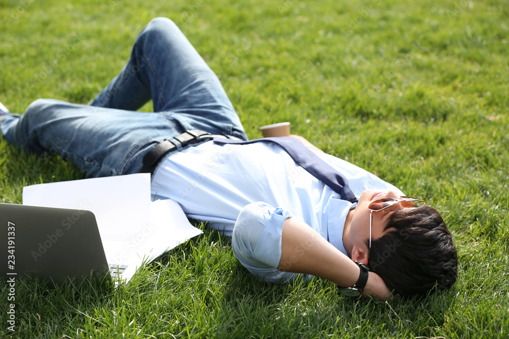 Young man lying on green lawn in park. Joy in moment Young man lying on green lawn in park. Joy in moment