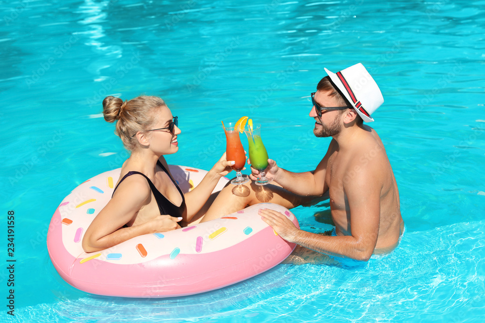 Fototapeta premium Young couple with refreshing cocktails and inflatable ring in swimming pool