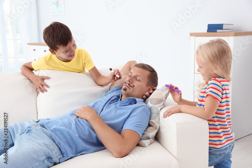 Little children painting their father's face while he sleeping on couch at home. April fool's day prank photo