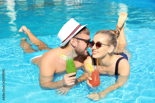 Young couple with refreshing cocktails in swimming pool at resort