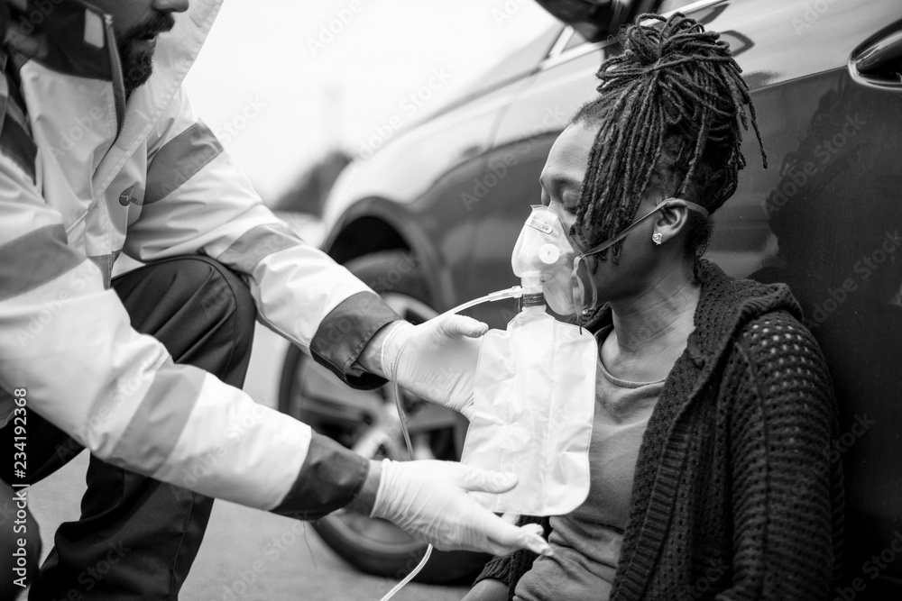 Male paramedic putting on an oxygen mask to an injured woman on a road