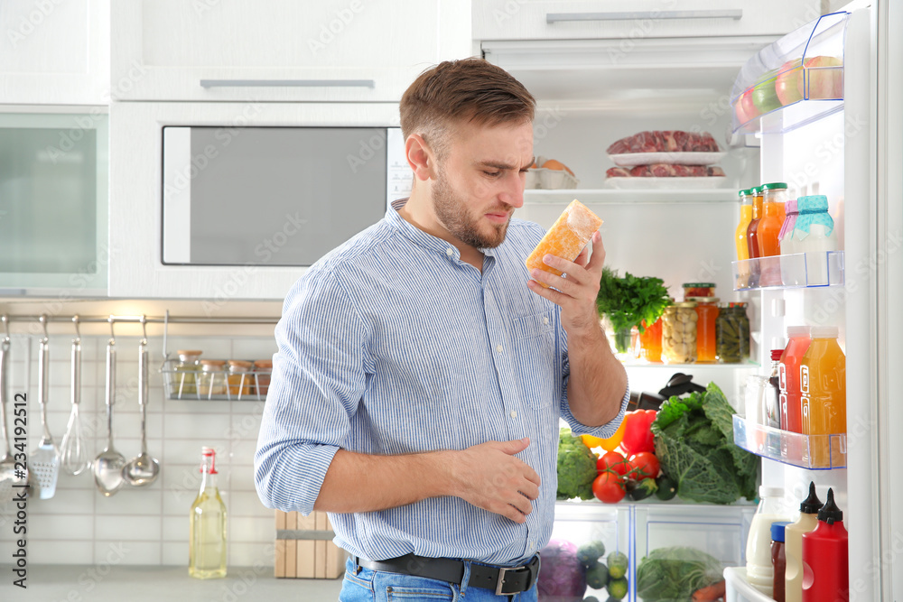Man feeling bad smell from stale cheese near refrigerator at home Man feeling bad smell from stale cheese near refrigerator at home