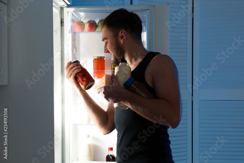 Man taking products out of refrigerator in kitchen at night photo