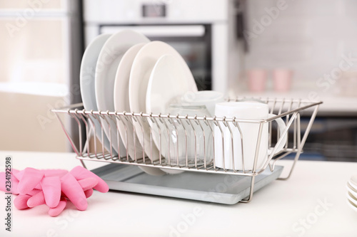 Dish drainer with clean dinnerware on table in kitchen photo