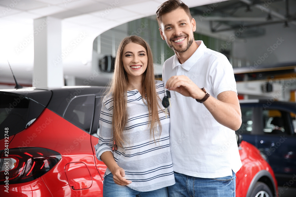 Happy woman and man with car keys in modern auto dealership Happy woman and man with car keys in modern auto dealership