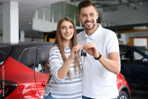 Happy woman and man with car keys in modern auto dealership