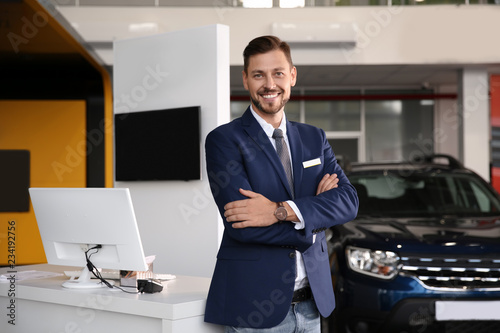 Salesman standing in modern auto dealership. Buying new car