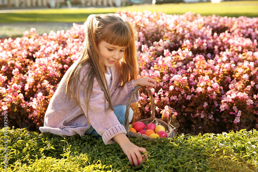 Fototapeta premium Cute little girl with basket of Easter eggs in park