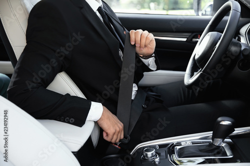 Driver fastening safety belt in luxury car, focus on hands