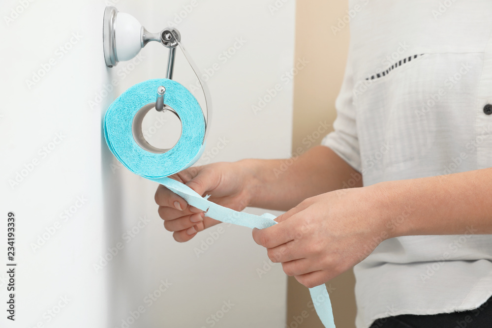 Woman taking toilet paper from roll holder in bathroom, closeup Woman taking toilet paper from roll holder in bathroom, closeup