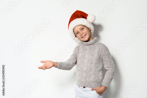 Cute little boy in warm sweater and Christmas hat on white background
