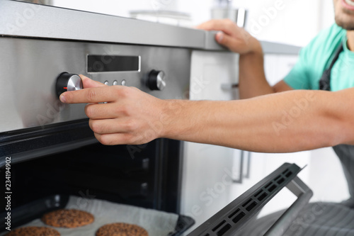 Young man baking cookies in oven at home, closeup