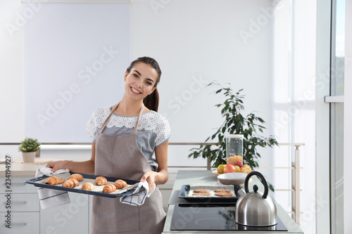 Young woman holding oven sheet with homemade croissants in kitchen