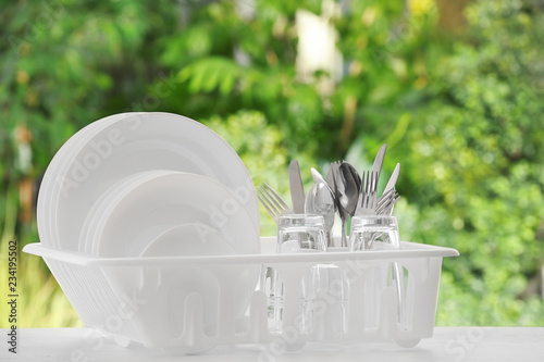 Set of clean dishes, glasses and cutlery on table against blurred background