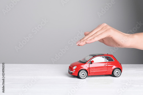 Insurance agent covering toy car on table, closeup. Space for text