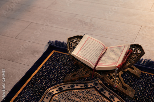 Rehal with open Quran and Muslim prayer beads on rug indoors. Space for text