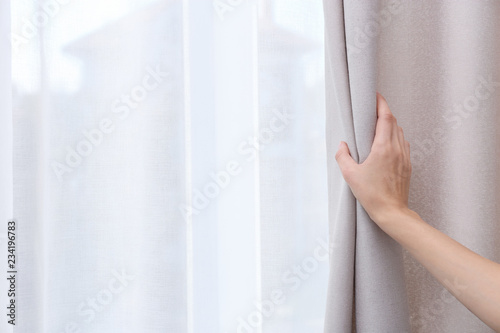 Woman opening window curtains at home, closeup. Space for text