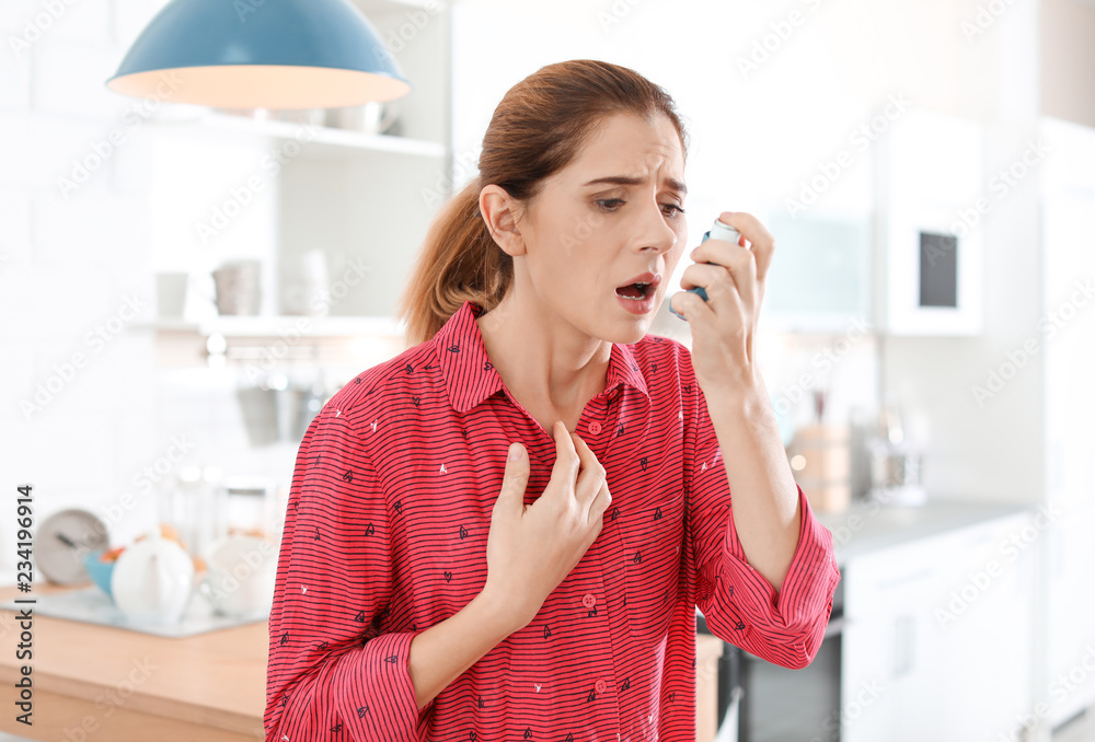 Young woman using asthma inhaler in kitchen Young woman using asthma inhaler in kitchen