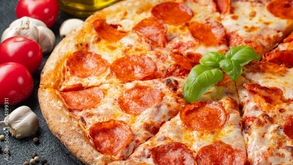 Tasty pepperoni pizza and cooking ingredients tomatoes basil on black concrete background