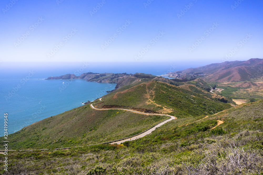 Beautiful views of the green hills of Marin Headlands crossed by a winding road; the Pacific Ocean coastline in the background; north San Francisco bay area, California Beautiful views of the green hills of Marin Headlands crossed by a winding road; the Pacific Ocean coastline in the background; north San Francisco bay area, California