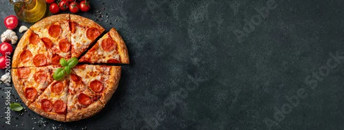 Obraz  z motywem Tasty pepperoni pizza and cooking ingredients tomatoes basil on black concrete background. Top view of hot pepperoni pizza. With copy space for text. Flat lay. Banner
