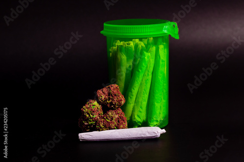 Obraz na płótnie A bright transparent green RX pill bottle filled with marijuana joints next to a pile of buds with long red hairs and a joint laying in front. w salonie