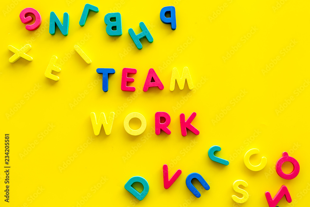 Fototapeta premium Teamwork training concept. Text teamwork lined with colored letters near toy letters on yellow background top view copy space