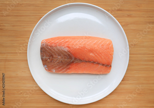 Raw piece of sliced salmon on white plate against wooden board background.