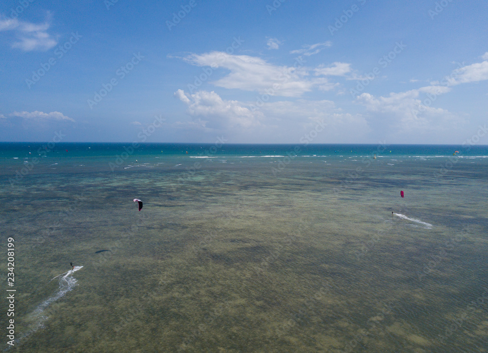 Kiteboarding, kite surf. Extreme sport kitesurfing in tropical blue ocean, clear beach. Aerial views, top view from drone of kitesurfing on the waves of the beautiful sea. Kite surfer rides the waves