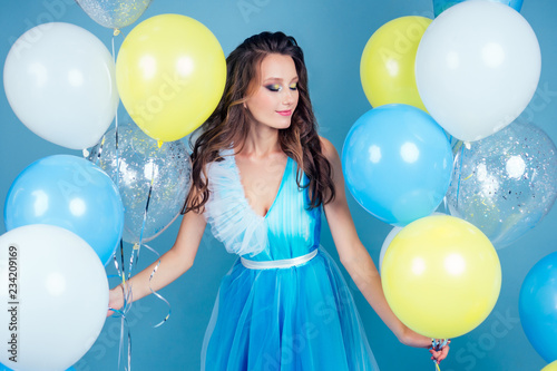 Gorgeous woman with curly hair in a long elegant dress butterfly having fun on party blue background studio,makeup evening look.portrait of adorable birthday girl with yellow and white balloons.