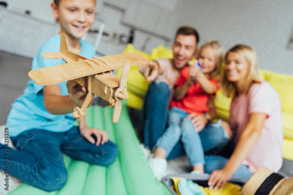 Obraz premium boy playing with toy wooden airplane with family having fun on background