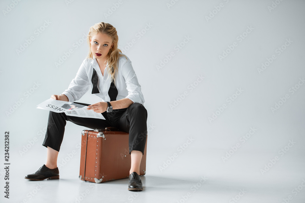 beautiful stylish girl reading business newspaper while sitting on vintage suitcase on grey beautiful stylish girl reading business newspaper while sitting on vintage suitcase on grey