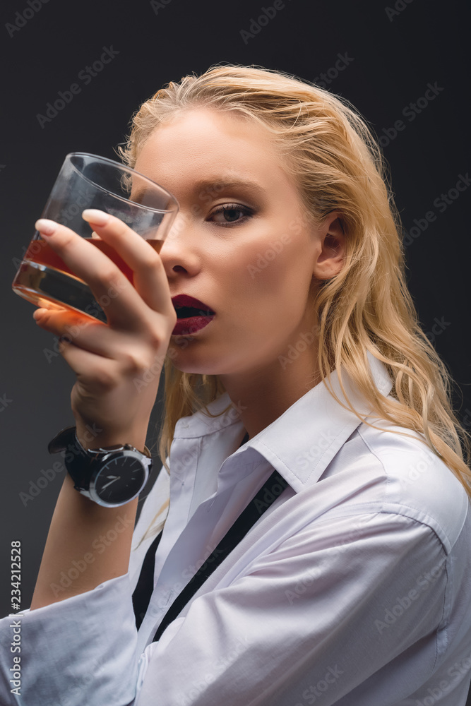 beautiful elegant girl in formal wear holding glass of whiskey, isolated on dark grey beautiful elegant girl in formal wear holding glass of whiskey, isolated on dark grey
