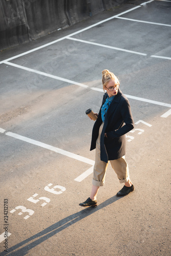 beautiful stylish girl with coffee to go walking on parking