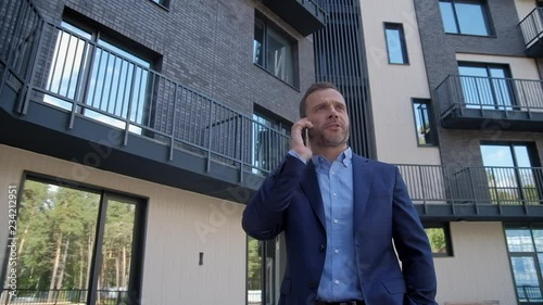 Wallpaper Mural Smiling man standing at residential luxury backyard and speaking at smartphone slow motion. Caucasian ambitious manager in suit wear selling living real estate at mobile speach outroor. Success leader Torontodigital.ca